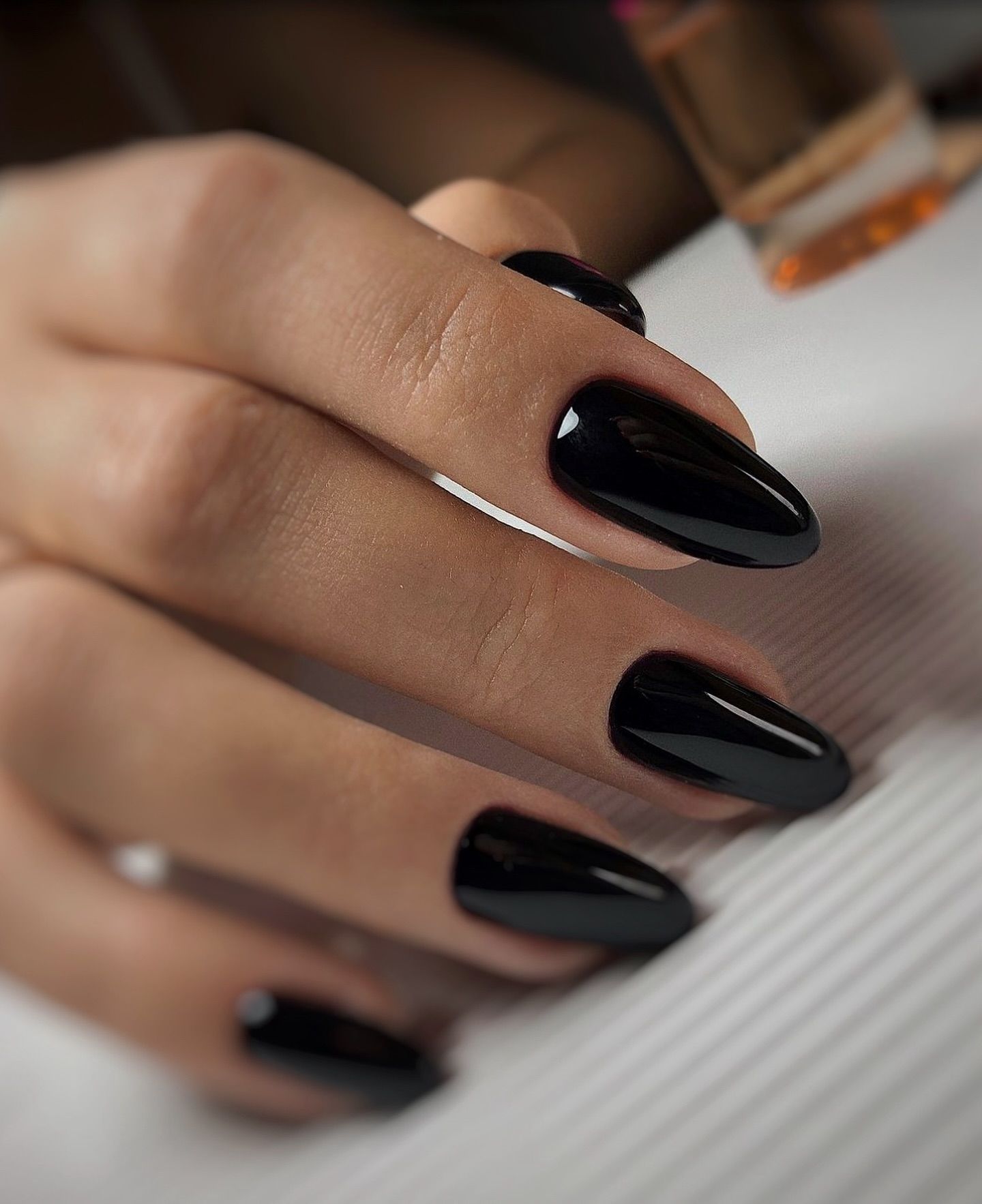 Głęboko czarny manicure w połysku na paznokciach o kształcie migdała.